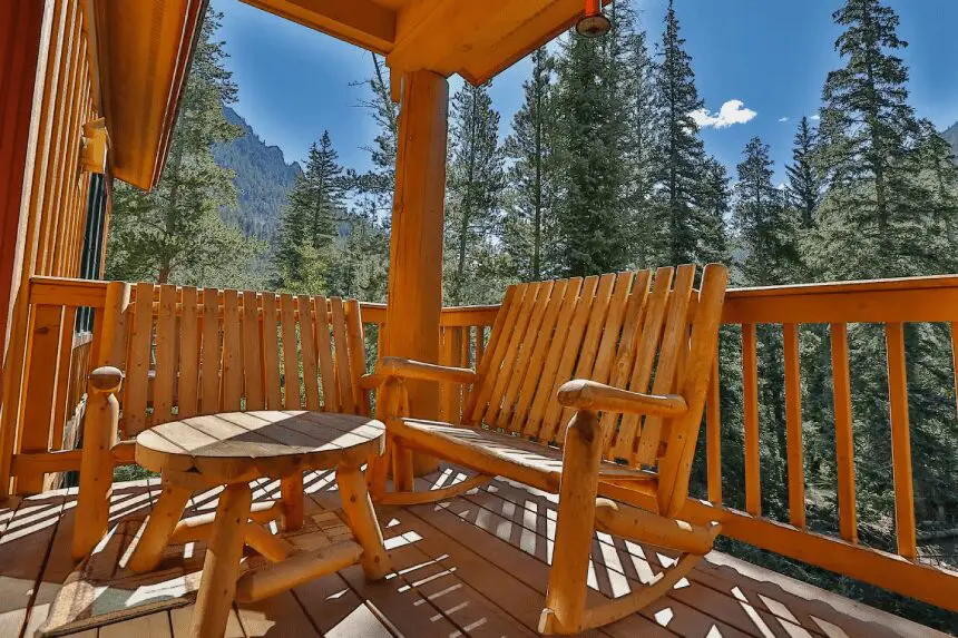 A wooden bench and table on the porch of a cabin.