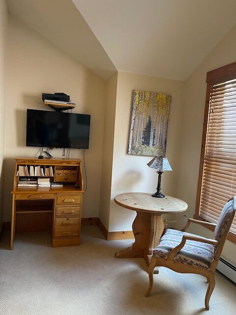 A room with a desk, chair and television.